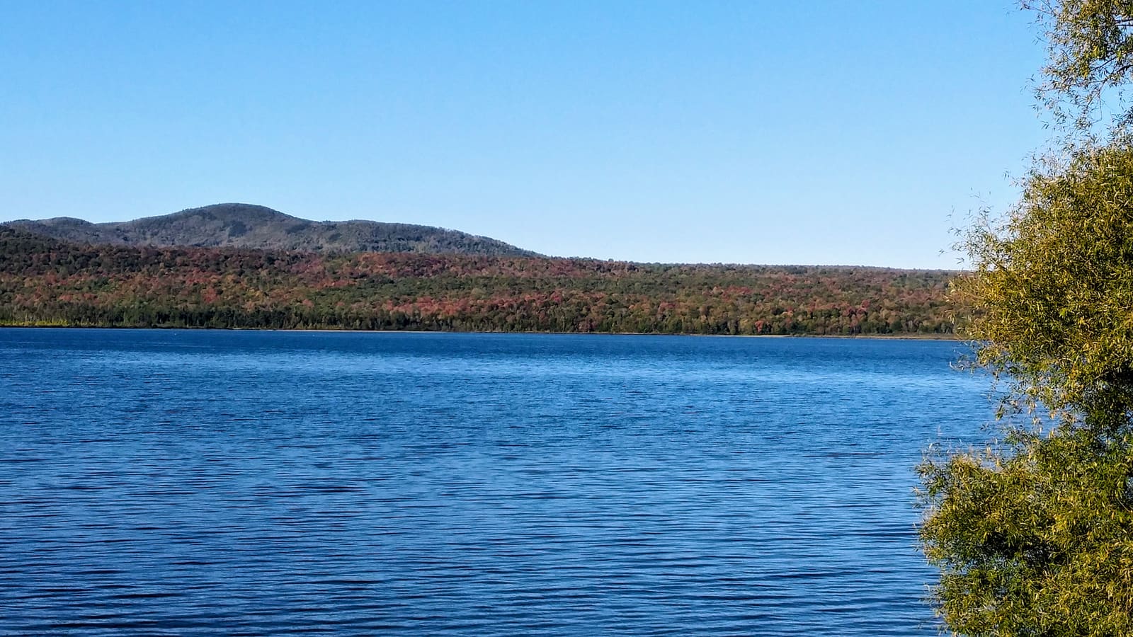 A calm blue lake below wooded hills turning red and gold in early fall